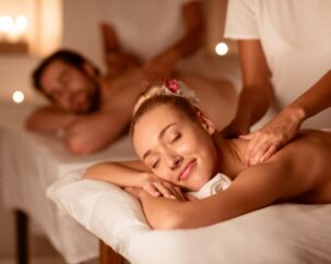 Couple Relaxing Receiving Back Massage Lying Closing Eyes At Romantic Luxury Spa With Burning Candles And Flowers. Wellness And Body Relaxation Therapy. Selective Focus, Low Light